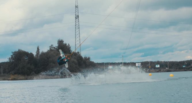 Attractive female practicing wakeboarding tricks in a wakepark near a city. 4K UHD 60 FPS 