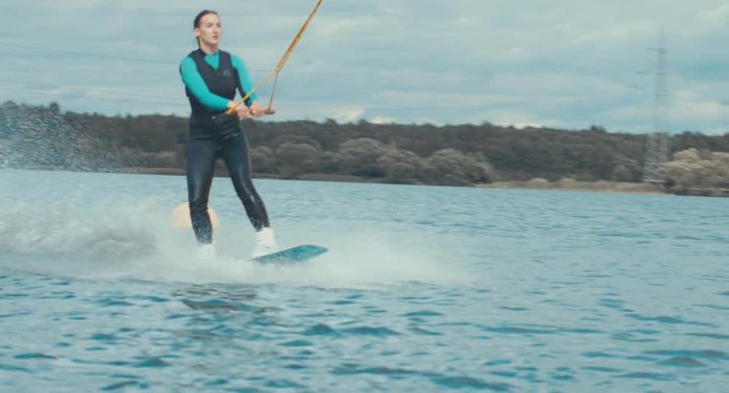 Attractive female practicing wakeboarding tricks in a wakepark near a city. 4K UHD 60 FPS 