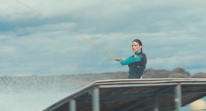 Attractive female wake boarding in a wakepark near a city. 4K UHD 60 FPS 