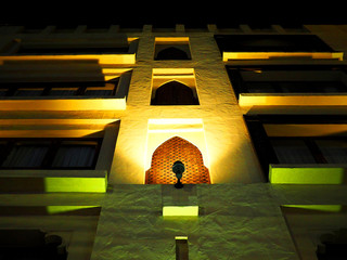 Dark night yellow spotlight light up on Indian style condominium building, arabian shape windows, stone wall, shadow, view from below