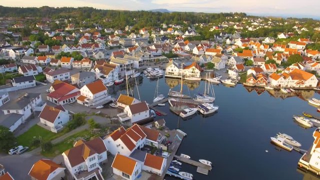 Top view of cozy port city Skudeneshavn, Norway. Beautiful white yachts and boats stand in the sea harbor. Amazing cityscape. Flight over roofs of houses, urban infrastructure, green gardens and roads