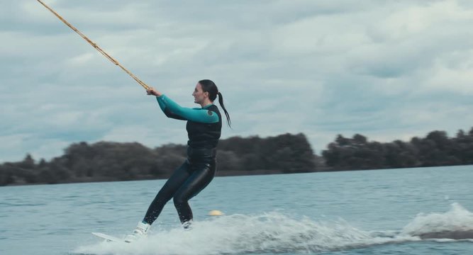 Attractive female wake boarding in a wakepark near a city. 4K UHD 60 FPS 