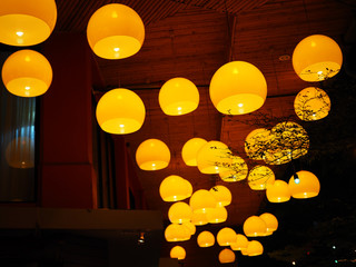 Orange yellow dome round glass unevenly hanging lighting lamp group cluster, from wooden roof, in the night, perspective