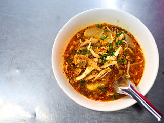 Top view of Thai local traditional spicy chicken piece with thin white rice noodle soup, left blank space, served in white plastic bowl, with spoon, on stainless steel table