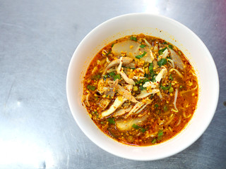 Top view of Thai local traditional spicy chicken piece with thin white rice noodle soup, left blank space, served in white plastic bowl, on stainless steel table