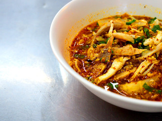 Part of Thai local traditional spicy chicken piece with thin white rice noodle soup, left blank space, served in white plastic bowl, on stainless steel table, close up shot