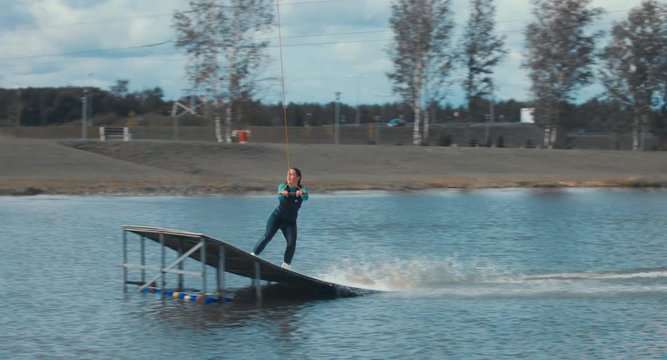 Attractive female practicing wakeboarding tricks in a wakepark near a city. 4K UHD 60 FPS 