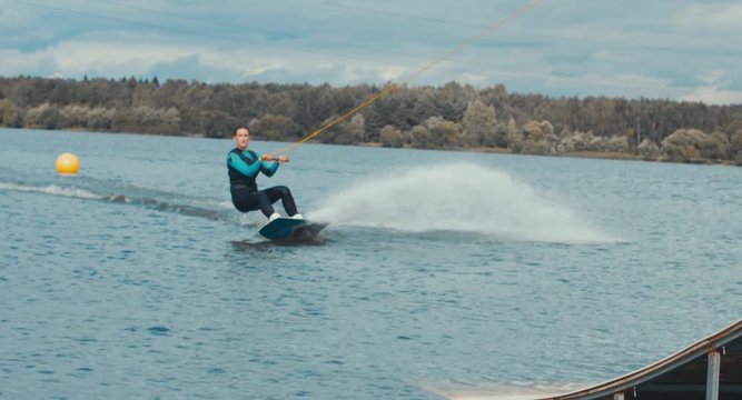 Attractive female practicing wakeboarding tricks in a wakepark near a city. 4K UHD 60 FPS 