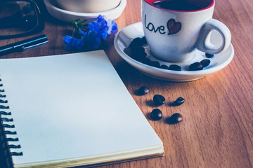 a sketchbook or a notebook on the brown wood  table with a cup of coffee and some coffee beans on the floor for background