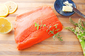Fresh portion of salmon with lemon, asparagus, butter and fresh herbs on a cutting board