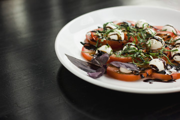 The Caprese salad on the white plate on black table