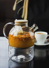 Sea buckthorn tea in the glass teapot. On the background of young blonde girl drinking tea in the cafe