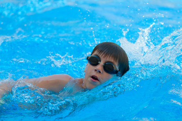 Fototapeta na wymiar Boy swimming freestyle in the pool/Teenager boy in black googles swimming freestyle in the swimming pool