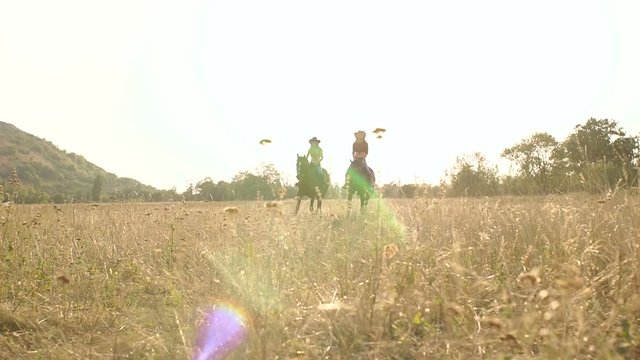 Silhouette of two slender girls on horseback in a field at sunset in countryside.