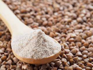 Buckwheat flour in wooden spoon and buckwheat grains. Whole-grain buckwheat flour on buckwheat grains background. Copy space.
