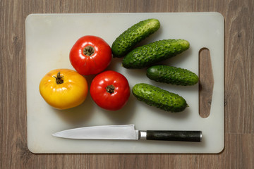 Tomato, cucumber and knife on cutting board.