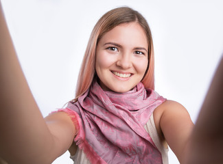 Fototapeta premium Portrait of a joyful casual girl taking selfie and holding camera with hands over white background