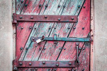 Vintage rustic wooden door secured with rusty metal latches and padlock closeup