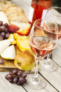 Two glasses of rose wine and board with fruits, bread and cheese on wooden table, shallow DOF