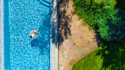 Fototapeta na wymiar Aerial view of girl in swimming pool from above, kid swim on inflatable ring donut and has fun in water on family vacation 