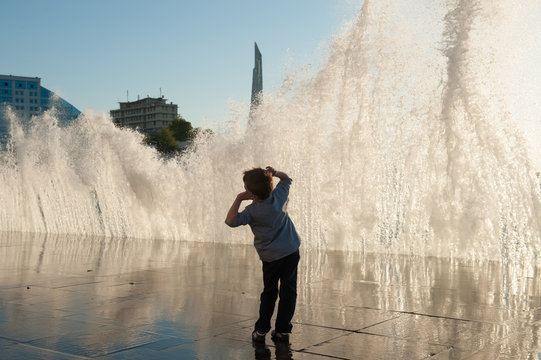 amazed small boy on a background of a giant wave on the city coast at sunset