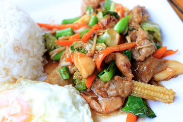 Delicious Thai dish chicken with stir fried vegetables in white dish with rice and fried egg on wooden table. Thai food.