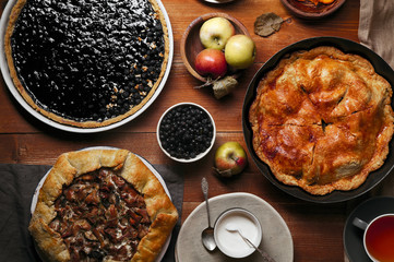 Traditional autumn pies arranged on red wooden rustic table. Chanterelle mushrooms, blueberry and sweet apple fillings. Top view.