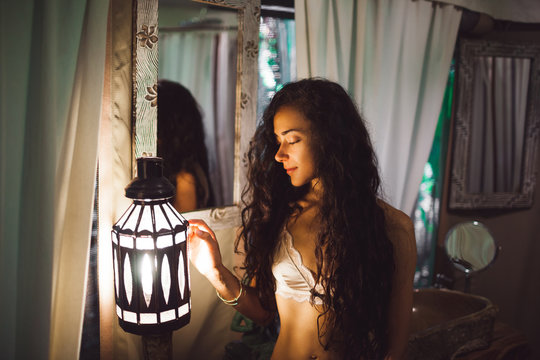 Beautiful sexy girl in white lingerie enjoying in amazing bathroom in Bali style. Handmade carving wooden furniture and lantern light