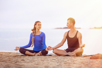 Fototapeta na wymiar Couple is practising yoga meditatin pose at tropical sunrise sea background.