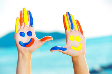 Closeup image of hands with colorful paint at blue summer outdoors background. Concept of happiness.