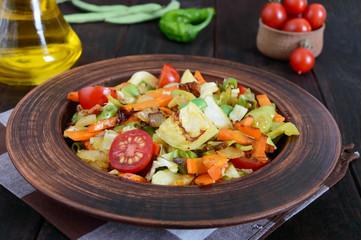 Vegetable stew of cabbage, green beans, carrots, tomatoes, onions, sweet peppers in a clay bowl on a dark wooden background. Warm salad. Vegetarian cuisine