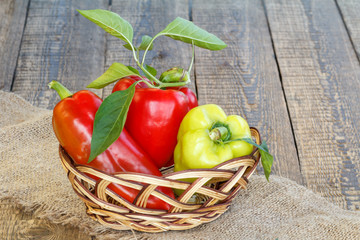 Fototapeta na wymiar Ripe red and yellow bell peppers in a wicker basket on piece of sackcloth.and wooden boards