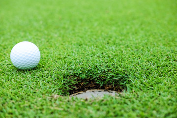 White color golf ball on green near hole at the morning time