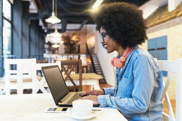 Beautiful afro american woman using mobile and laptop in the coffee shop.