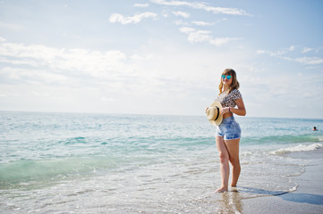 Beautiful model relaxing on a beach of sea, wearing on jeans short, leopard shirt and hat.