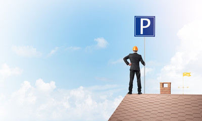 Young businessman with parking sign standing on brick roof. Mixed media