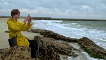 Young man sitting on shore filming waves phone slow motion