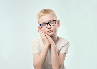 portrait of caucasian boy with blond hair. He is closing eyes and hold hands like pillow, wanting to sleep.