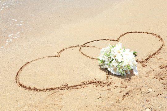 Beautiful bouquet and drawing of hearts on sand. Beach wedding concept