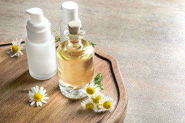 Bottles with cosmetic products and fresh chamomile flowers on wooden board