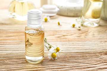 Bottle with essential oil and fresh chamomile flowers on wooden table