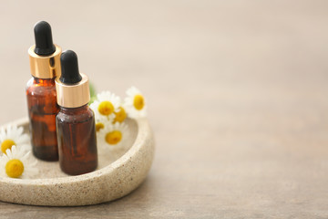 Bottles with essential oil and fresh chamomile flowers on stone coaster