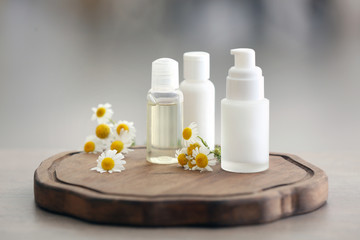 Fototapeta na wymiar Bottles with cosmetic products and fresh chamomile flowers on wooden board