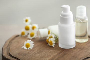 Fototapeta na wymiar Bottles with cosmetic products and fresh chamomile flowers on wooden board
