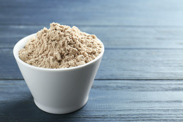 Bowl with protein powder on wooden background