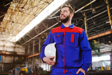 Builder or engineer with white construction helmet in hands on background of plant