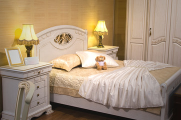 Luxury bedroom interior in vintage style. Empty photo frame on the bedside table. Teddy bear and white dress on the bed.