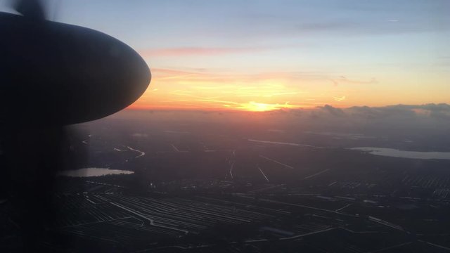 As the sun sets, a propeller plane, cruises over Amsterdam Airport (4K)