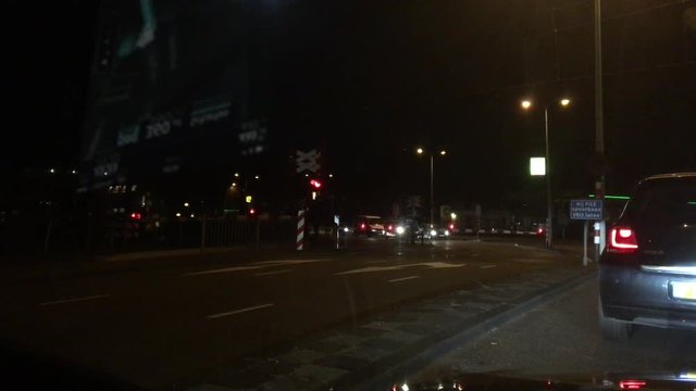 In the dark of an Amsterdam night, a car waits at a crossing as a train passes