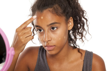 a young dark skinned woman applies a liqiud foundation on her face